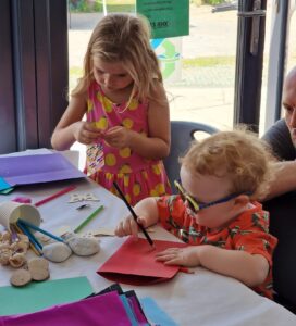 Two young girls crafting at a table with pencils and paper.