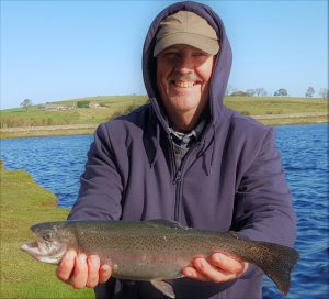 Man standing in front of Fontburn reservoir holding his catch of the day